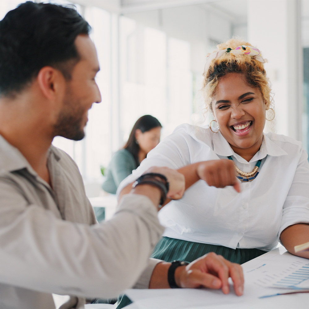 A happy woman with clear vision laughing and fist-bumping a colleague, representing the confidence and lifestyle benefits after LASIK surgery.