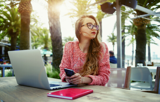Woman with glasses using phone and laptop outdoors